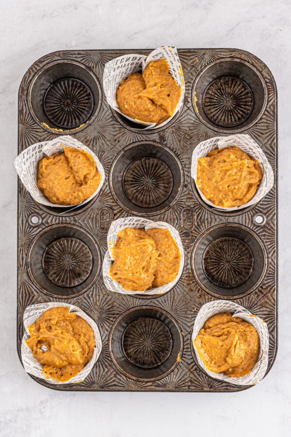 This bakery-style easy pumpkin muffin recipe creates moist and tender muffins made with a whole can of pumpkin and warm autumn spices! A muffin tin with every other well filled with liners and muffin batter.