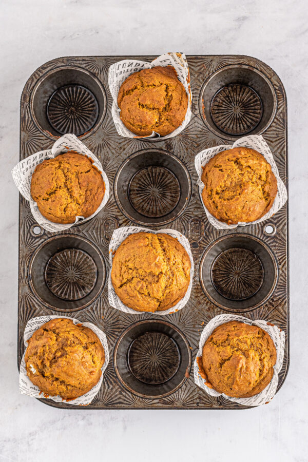 This bakery-style easy pumpkin muffin recipe creates moist and tender muffins made with a whole can of pumpkin and warm autumn spices! Baked pumpkin muffins in liners.