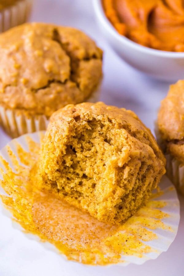 These Pumpkin Oatmeal Muffins are made easily in just one-bowl and are loaded with pumpkin flavor with a deliciously chewy consistency! A bite taken out of a pumpkin oatmeal muffin sitting on a muffin liner.