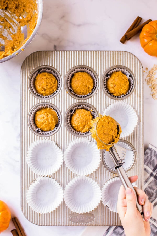 These Pumpkin Oatmeal Muffins are made easily in just one-bowl and are loaded with pumpkin flavor with a deliciously chewy consistency! Muffin batter being scooped into a muffin tin.