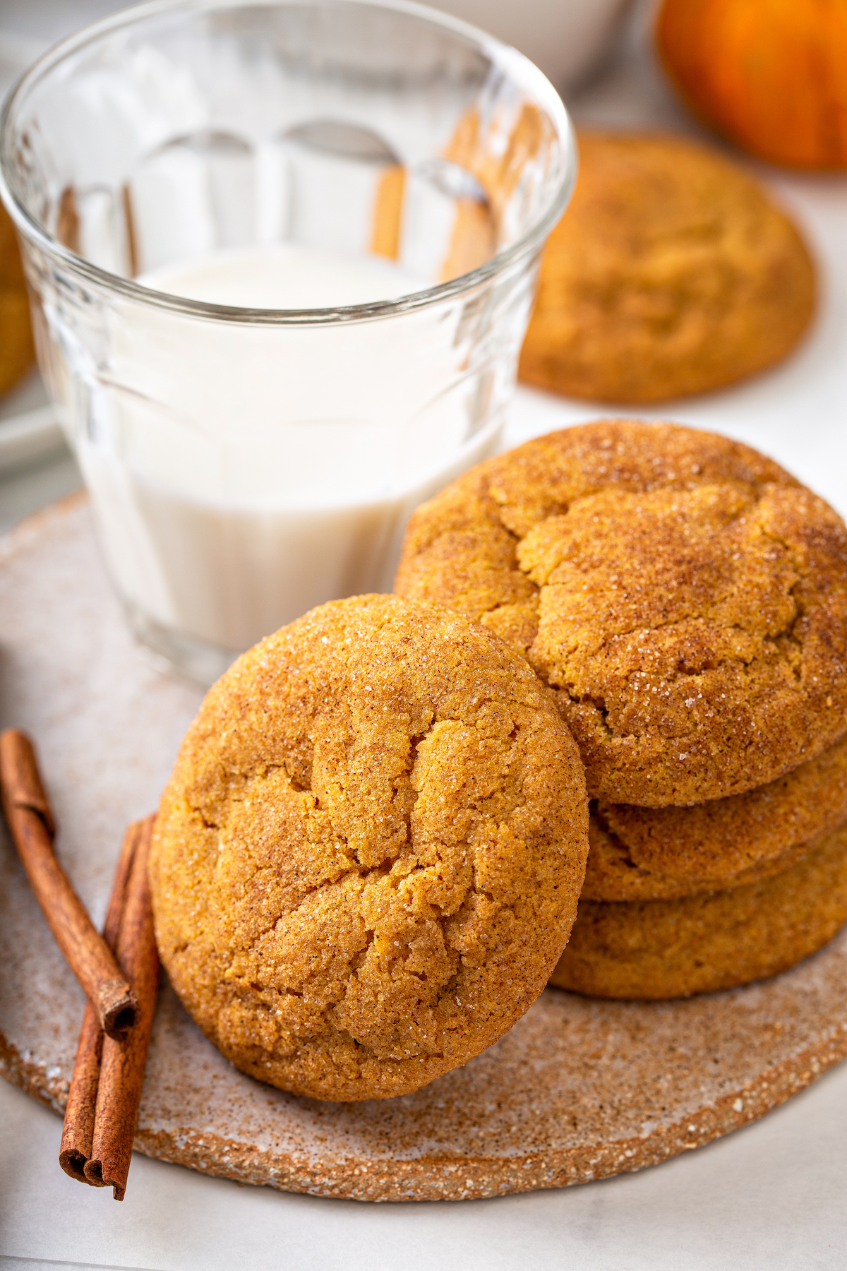 Pumpkin snickerdoodles, coated in sweet cinnamon sugar, are the perfect cookie recipe for fall! These easy pumpkin cookies are so addicting! Stack of sugary pumpkin snickerdoodles next to a glass of milk.