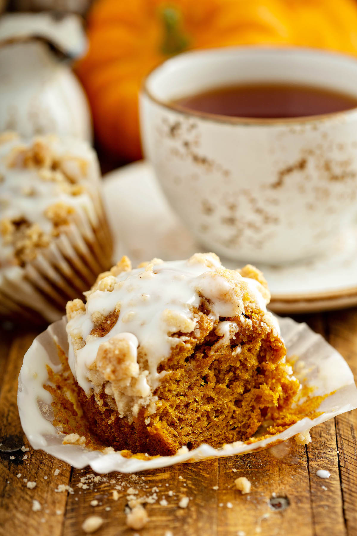 Moist, pumpkin streusel muffins are perfectly spiced with a crumbly cinnamon streusel topping and an optional drizzle of cream cheese icing! Pumpkin muffin with the liner removed and a bite taken out of the muffin.