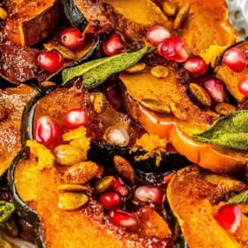 Close-up of roasted acorn squash slices topped with pomegranate seeds, roasted pumpkin seeds, and herbs.
