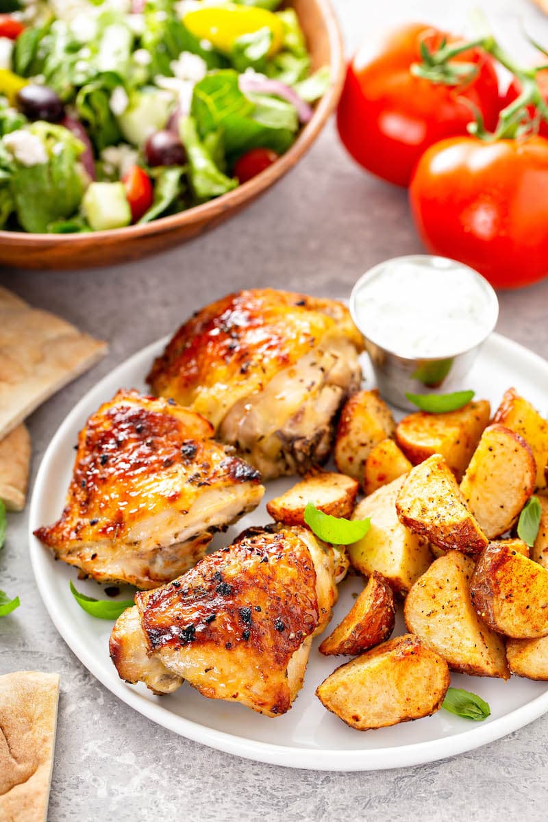 This is the best oven baked chicken recipe! Bone-in chicken breasts or thighs marinated and baked in the oven with a garlicky, citrus glaze. Perfectly baked chicken on a white plate with roasted potatoes.