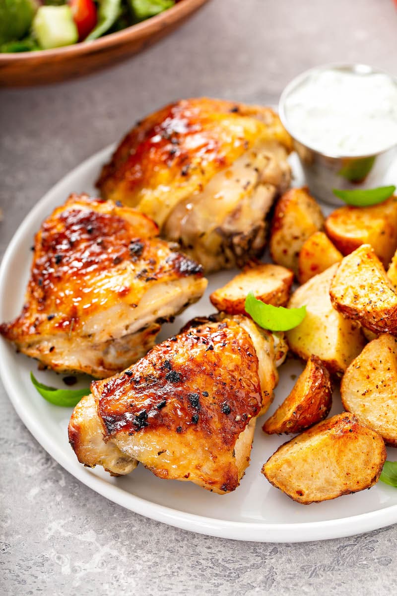 This is the best oven baked chicken recipe! Bone-in chicken breasts or thighs marinated and baked in the oven with a garlicky, citrus glaze. Perfectly baked chicken on a white plate with roasted potatoes.