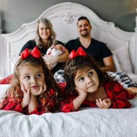 Two Twin Girls Laying on a Bed with their Mom, Dad and Newborn Brother in the Background