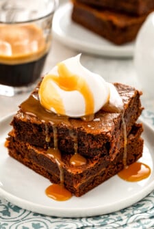 A stack of two salted caramel brownies with a caramel drizzle and whipped cream on top.