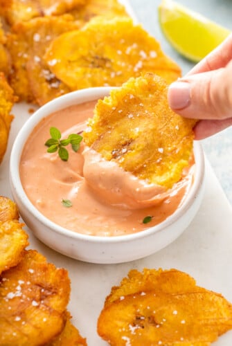 Tostones being dipped into a bowl of mayo ketchup.