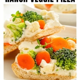 A slice of crescent roll veggie pizza topped with broccoli, cauliflower, carrot slices, and herbs on a white plate, with another slice in the background.