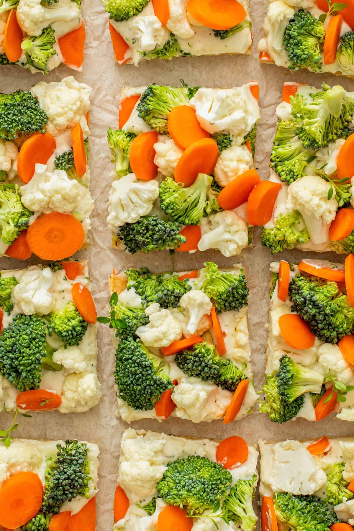 This easy Crescent Roll Veggie Pizza is a classic appetizer made with fresh crunchy veggies and a layer of tangy ranch and cream cheese. Rectangular crescent roll veggie pizza slices topped with fresh broccoli, cauliflower, and carrot rounds are arranged on a sheet of parchment paper.
