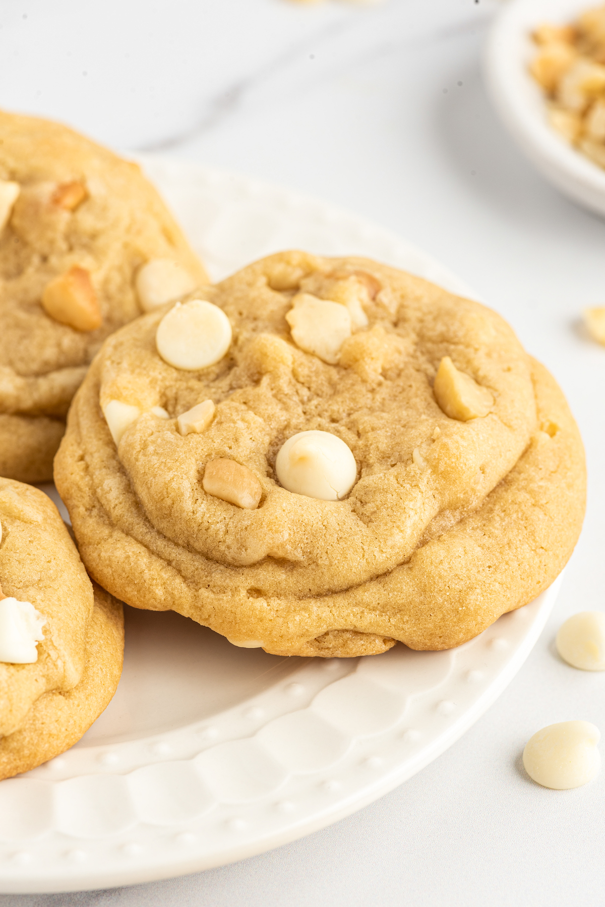Salty-sweet White Chocolate Macadamia Nut Cookies have the perfect balance of chew and crunch. The best white chocolate chip cookies! A close-up shot of a cookie with white chocolate chips and macadamia nuts.