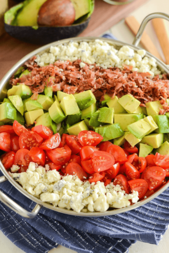 Copycat Maggianos Chopped Salad - blue cheese, tomatoes, avocados, bacon in a silver serving dish on a blue and white cloth